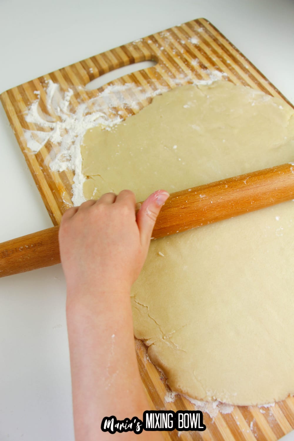 dough being rolled out with a wooden rolling pin on a cutting board