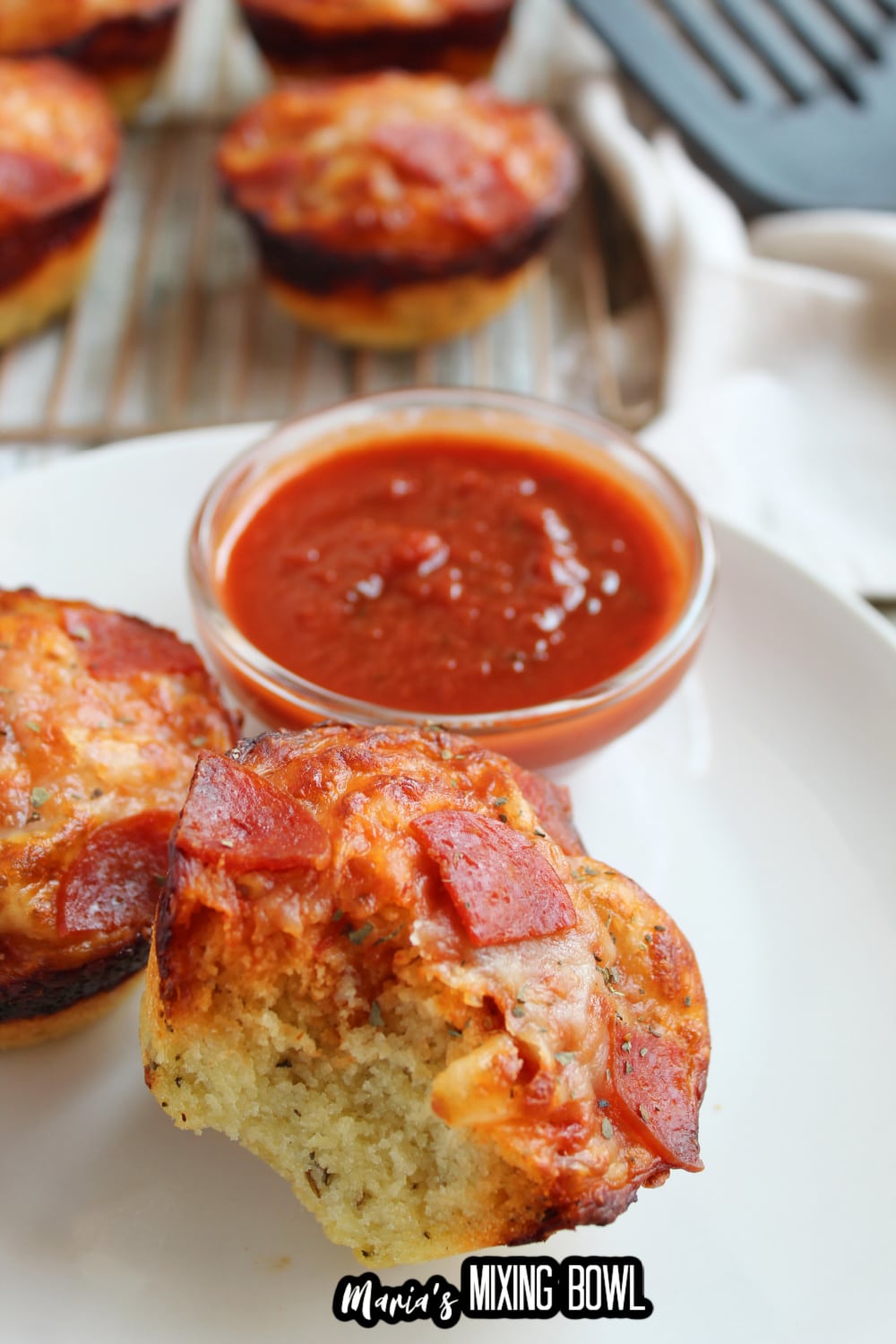 two deep dish pepperoni bites on a white plate with small bowl of pizza sauce