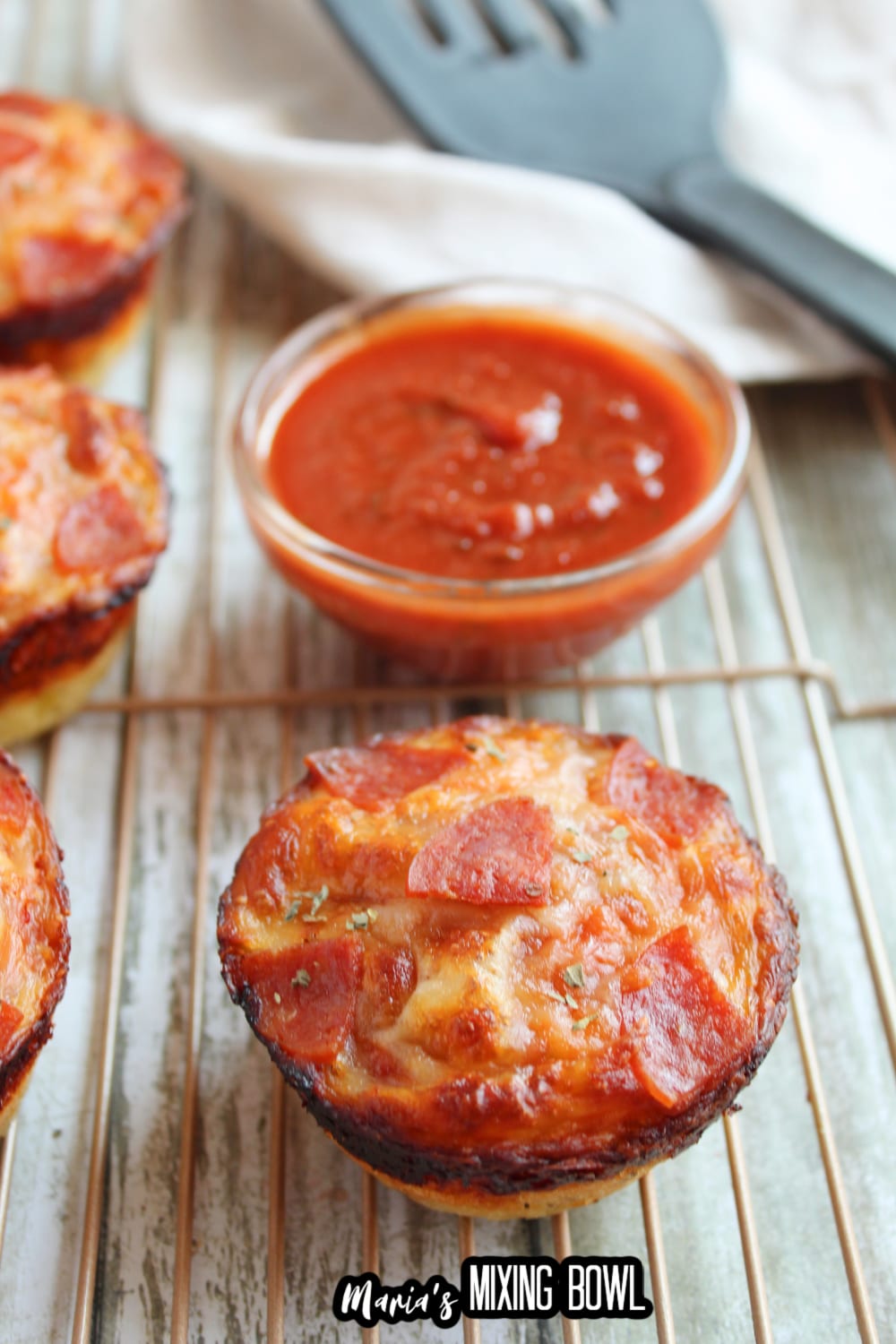 single pizza bite on a wire cooling rack with a small glass bowl filled with pizza sauce