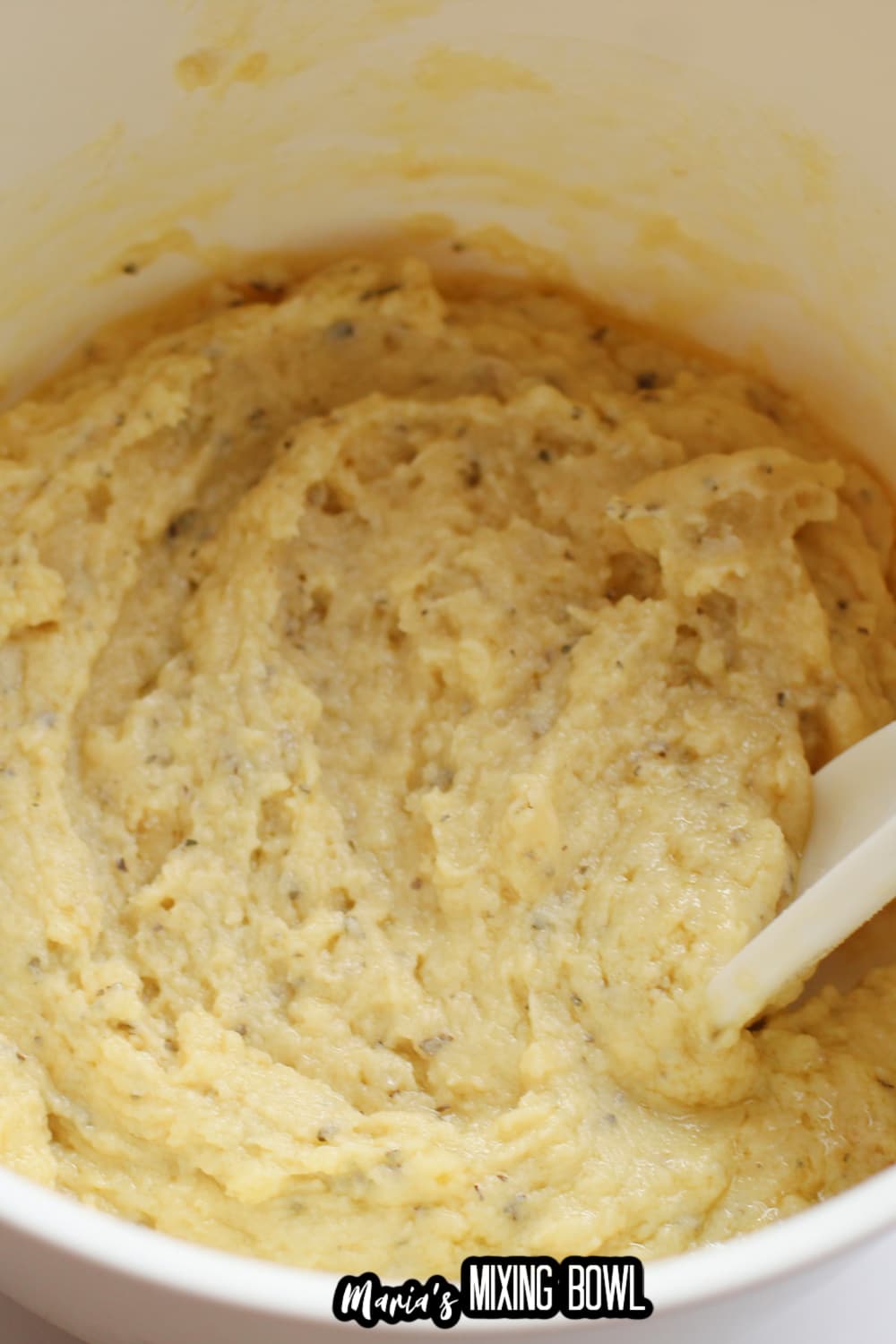 dough being mixed in a white mixing bowl with a white spoon