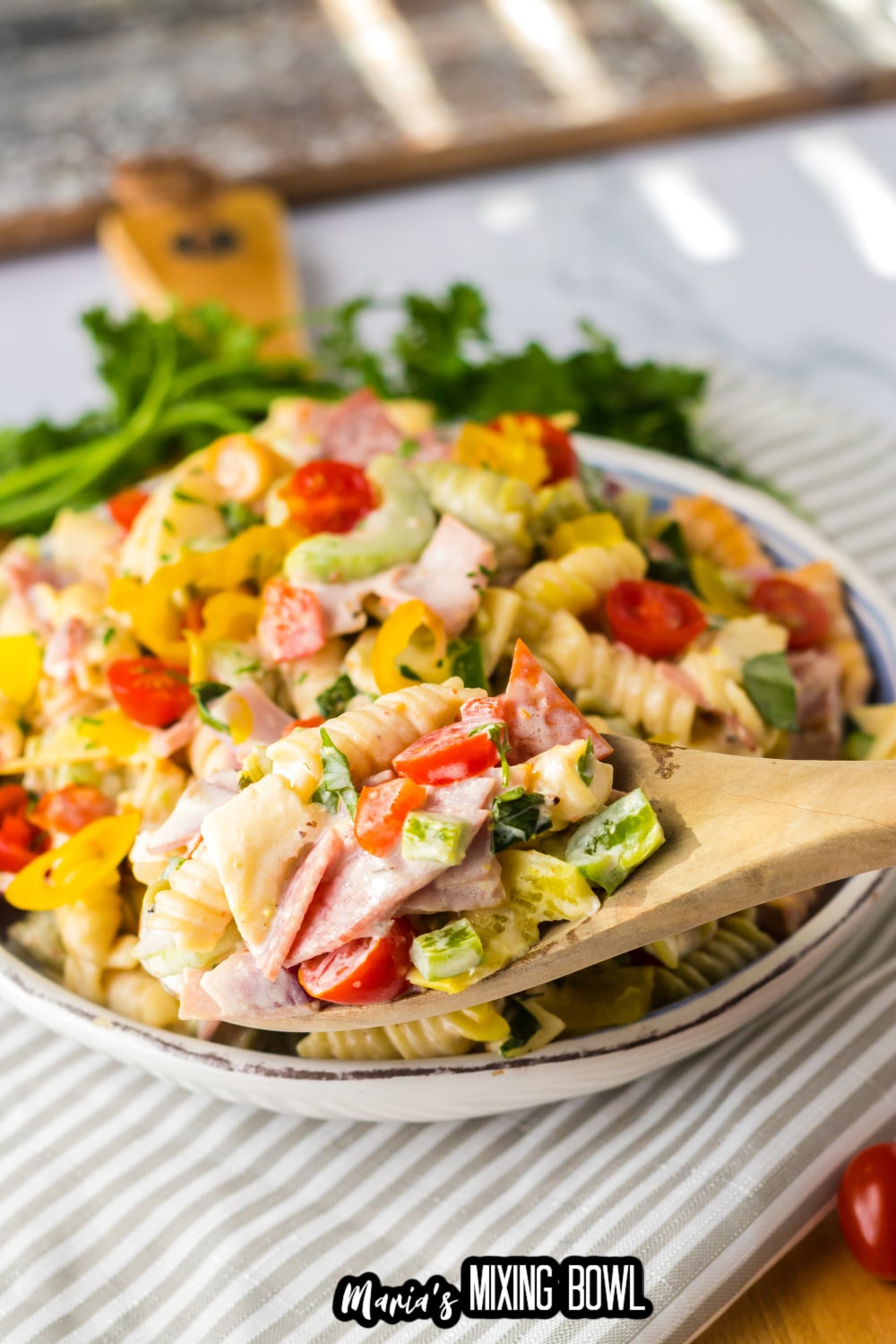 italian sub pasta salad in a white and blue bowl with a wooden spoon