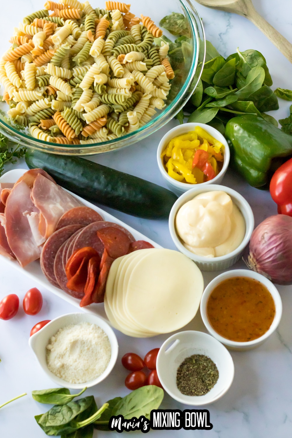 pasta, cucumber, peppers, onion, mayo, meat, cheese, and seasoning on a white background