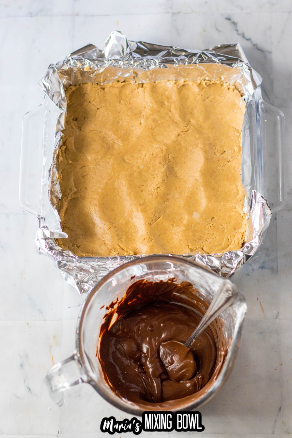 peanut butter being pressing into a baking dish lined with foil