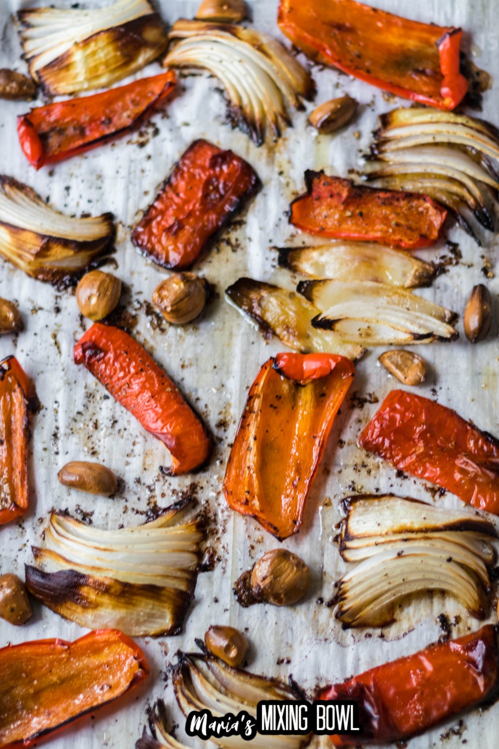roasted peppers, onions, and garlic on a parchment lined baking sheet