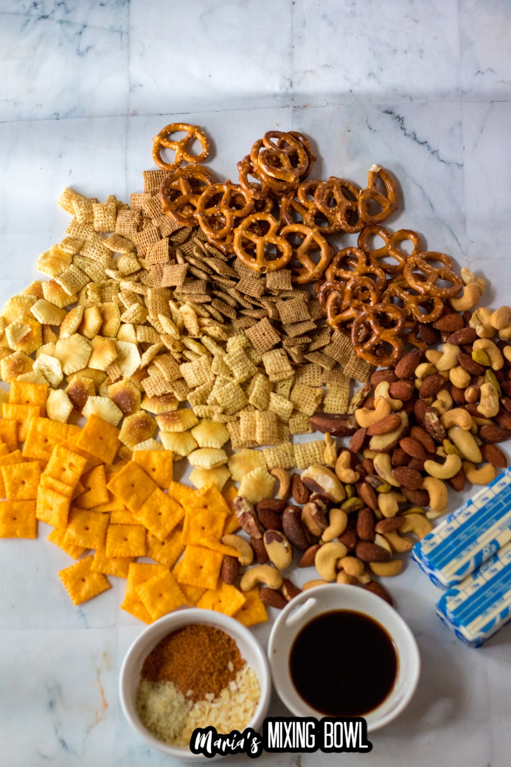 pretzels, chex ceral, butter, mixed nuts, seasonings, oyster crackers, and cheez its on a marble backdrop