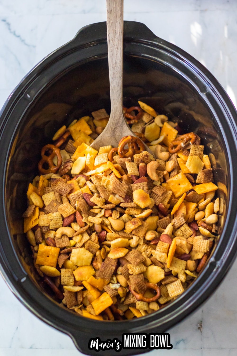 crock pot filled with slow cooker chex mix with a wooden spoon in it