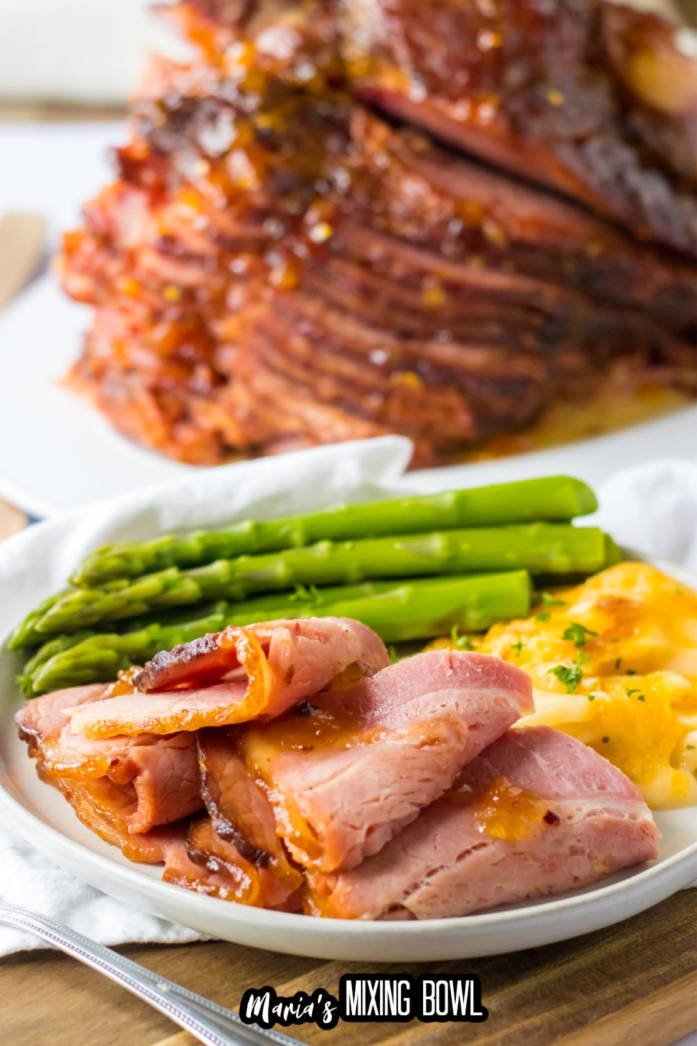 close up of slices of hot honey ham on a white plate with asparagus and au gratin potatoes