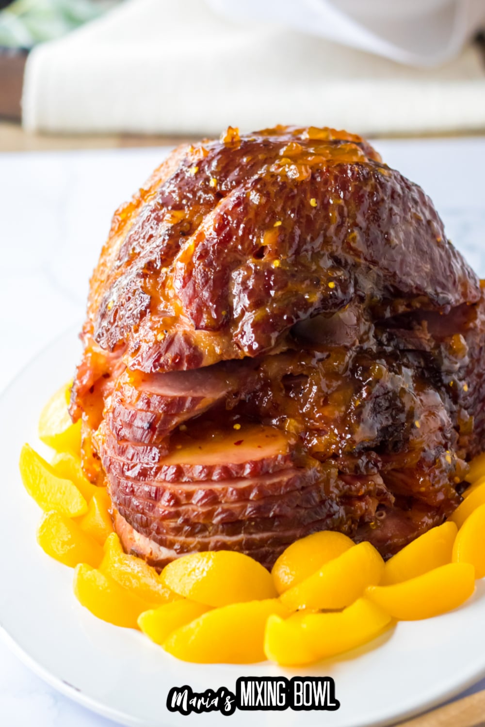 finished ham on a white serving platter surrounded by peaches