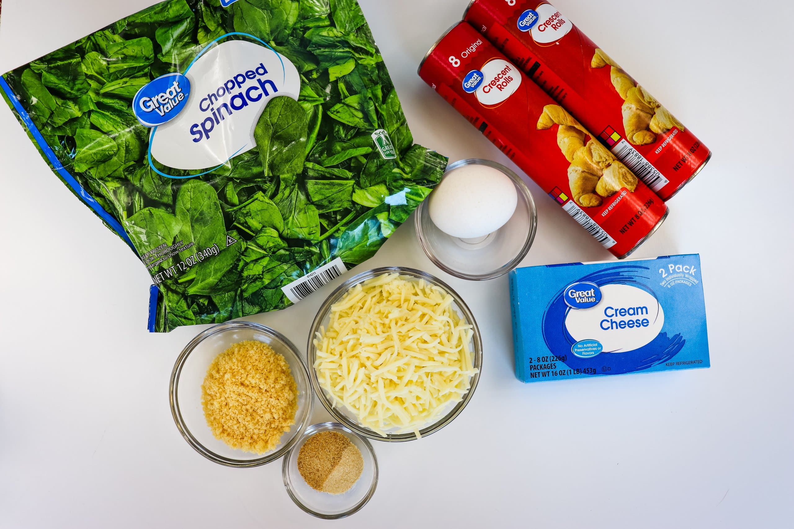 spinach, cans of crescent rolls, cheese, cream cheese, egg and seasonings on a white background.