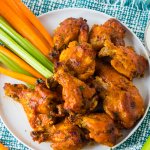 stack of chicken wings on a white plate with celery and carrot sticks