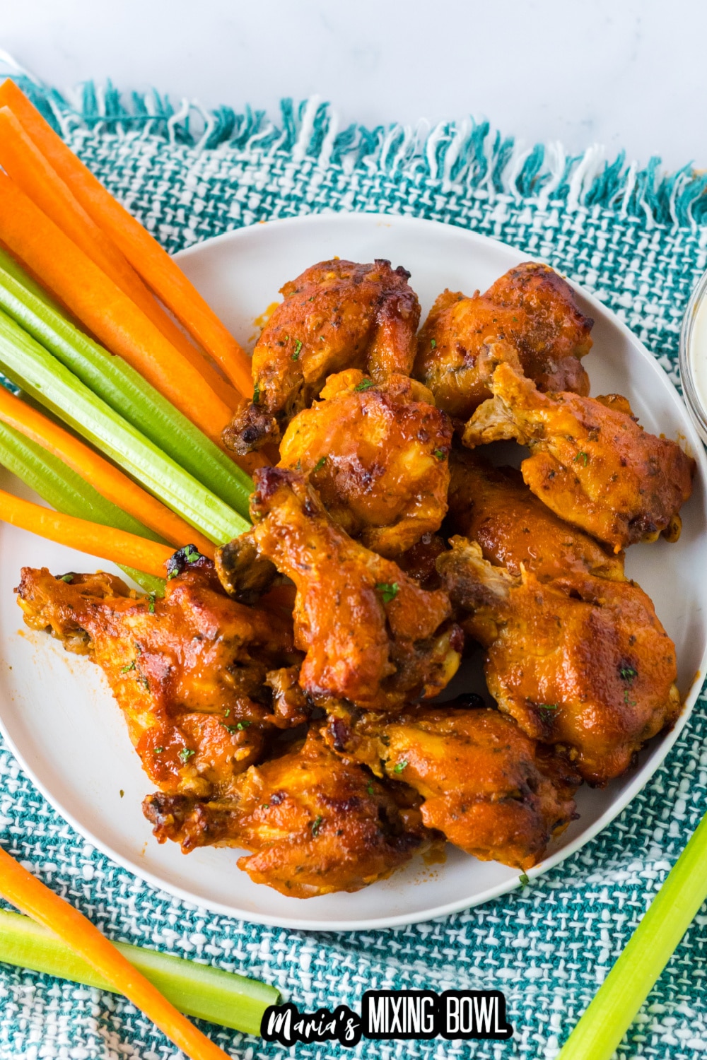 stack of chicken wings on a white plate with celery and carrot sticks