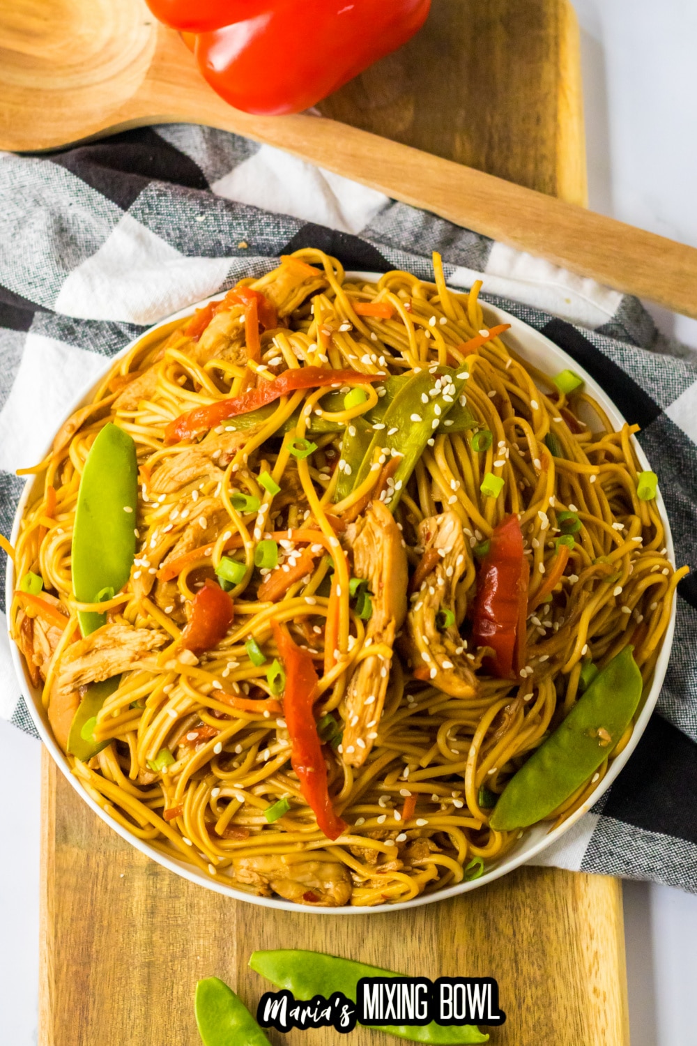 white plate filled with chicken lo mein and a bell pepper in the background