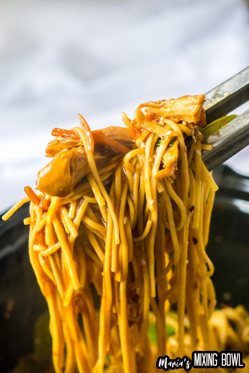 bite of chicken lo mein held in the air between two chop sticks
