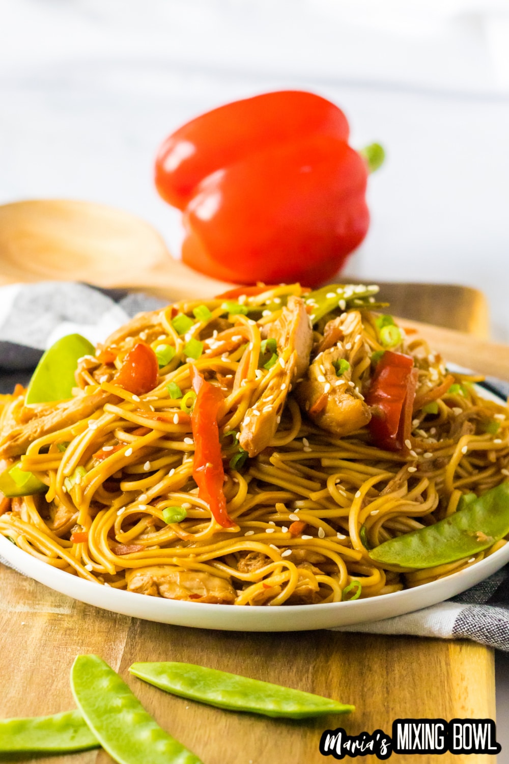 white plate filled with chicken lo mein and a bell pepper in the background