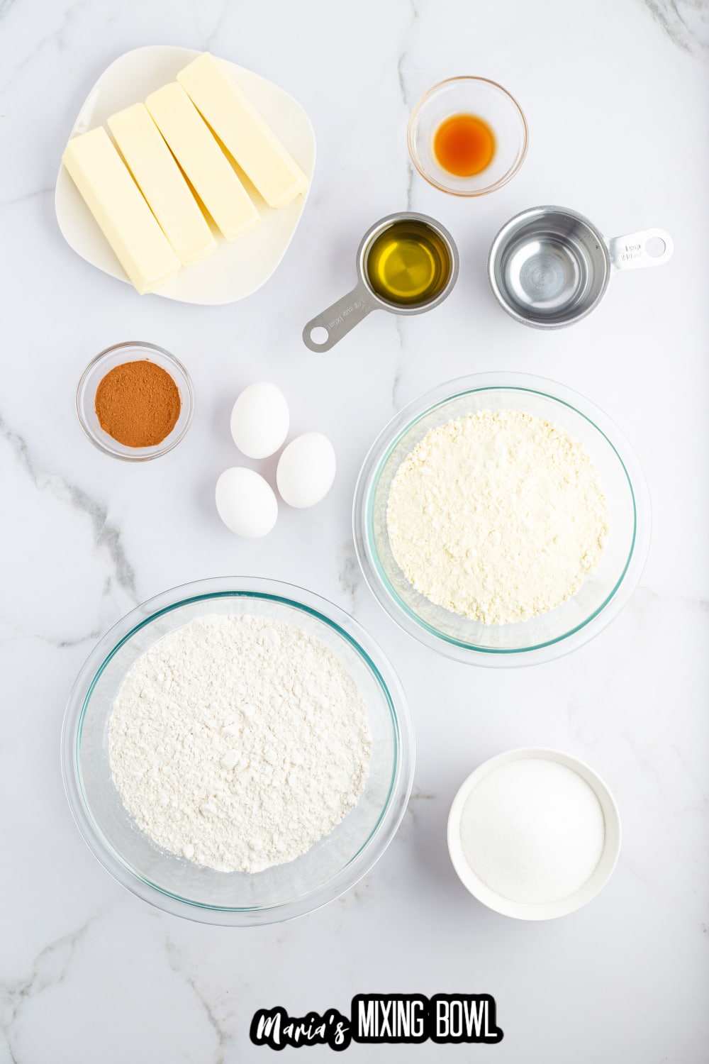 butter, vanilla, oil, cinnamon, eggs, flour, and sugar on a white marble background
