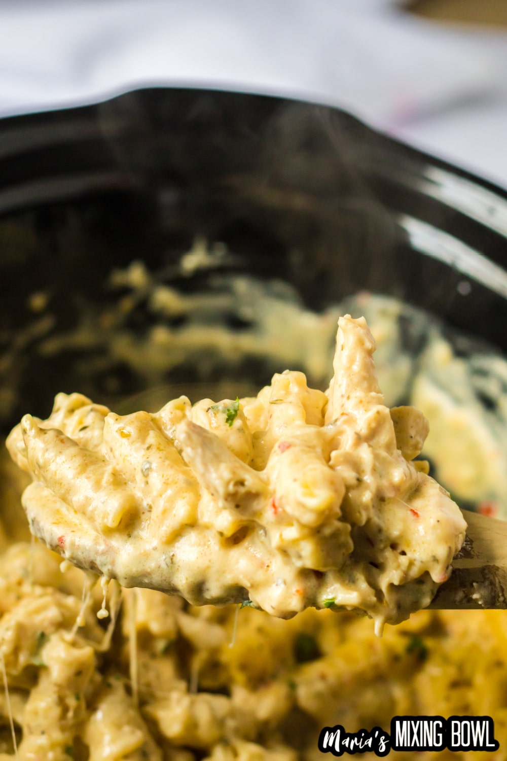 spoon full of chicken pasta held in the air before a slow cooker