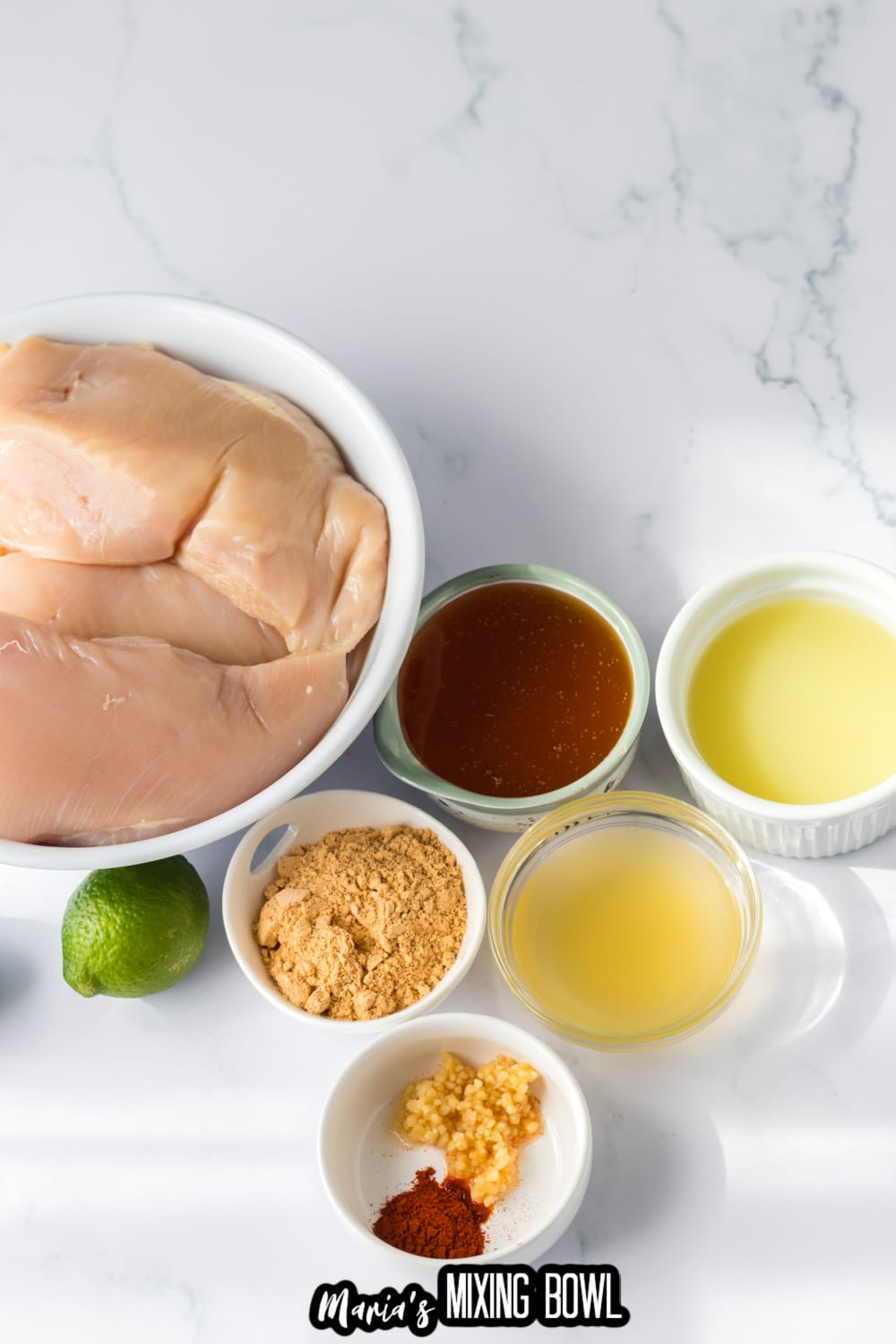 chicken breasts, garlic, honey, lime juice, and seasoning on a white marble backdrop