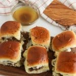 six italian beef sliders on a wooden cutting board with a bowl of au jus in the background