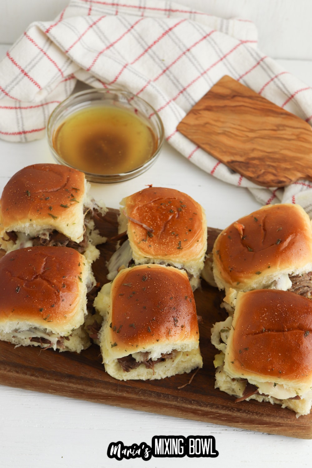 six italian beef sliders on a wooden cutting board with a bowl of au jus in the background