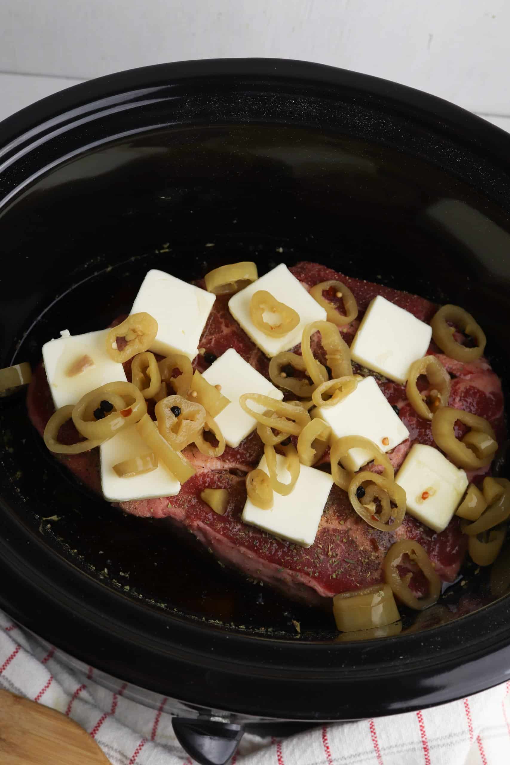 chuck roast, butter, and peppers in a slow cooker
