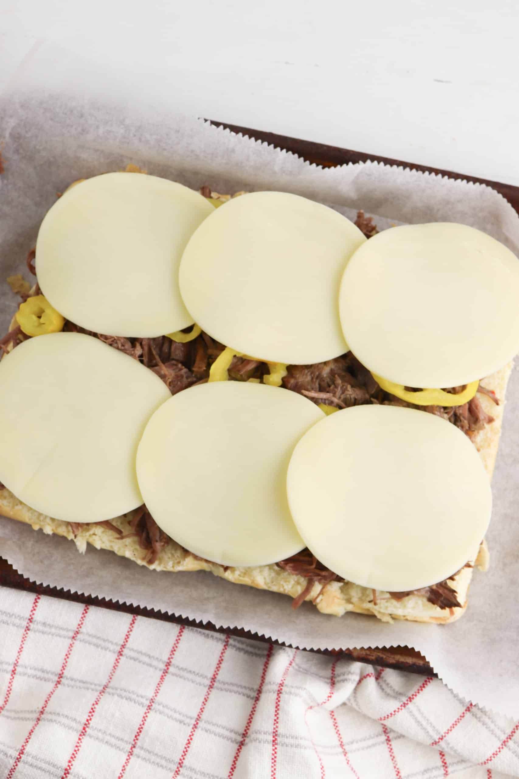 beef, peppers and cheese on sub rolls on a parchment lined baking sheet