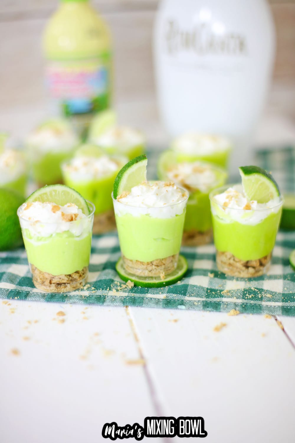 key lime pie shots on a green and white napkin with a bottle of lime juice and rum chata in a background