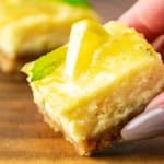 slice of lemon cheesecake bars held in a woman's hand.