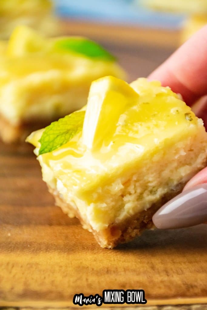 slice of lemon cheesecake bars held in a woman's hand.