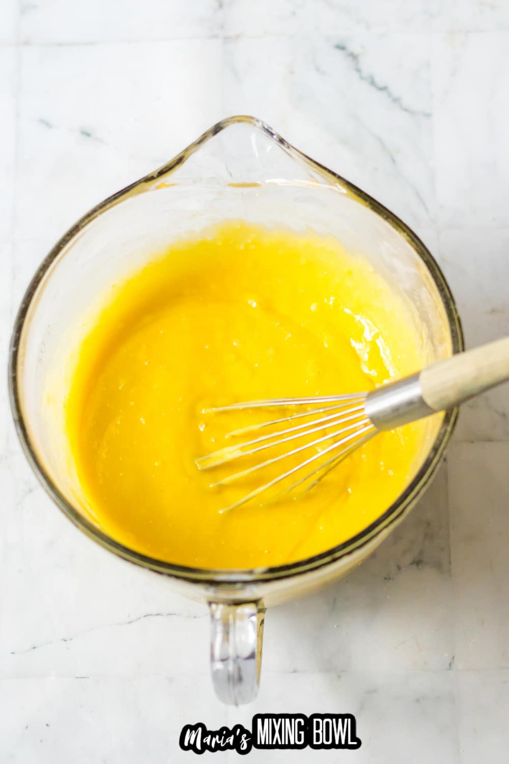 lemon cake batter being mixed with a whisk in a large glass measuring cup