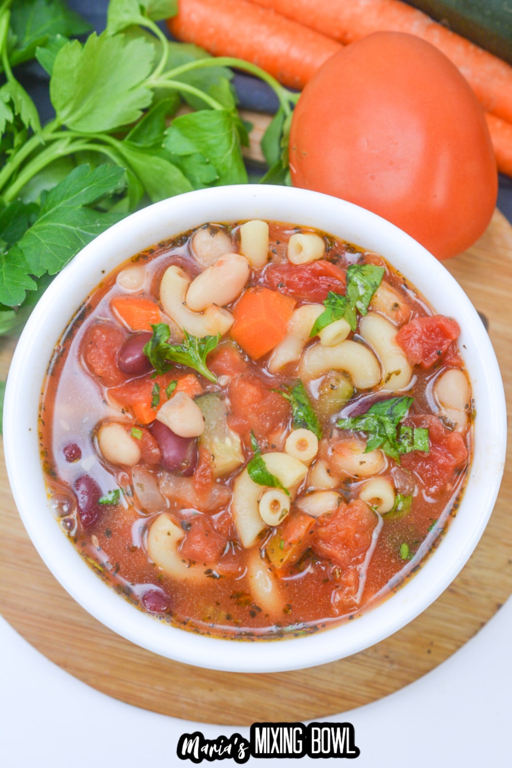 white bowl on a wooden hot pad filled with minestrone soup