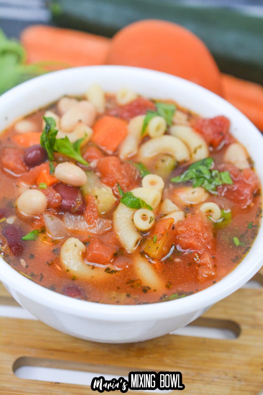 white bowl on a wooden hot pad filled with minestrone soup
