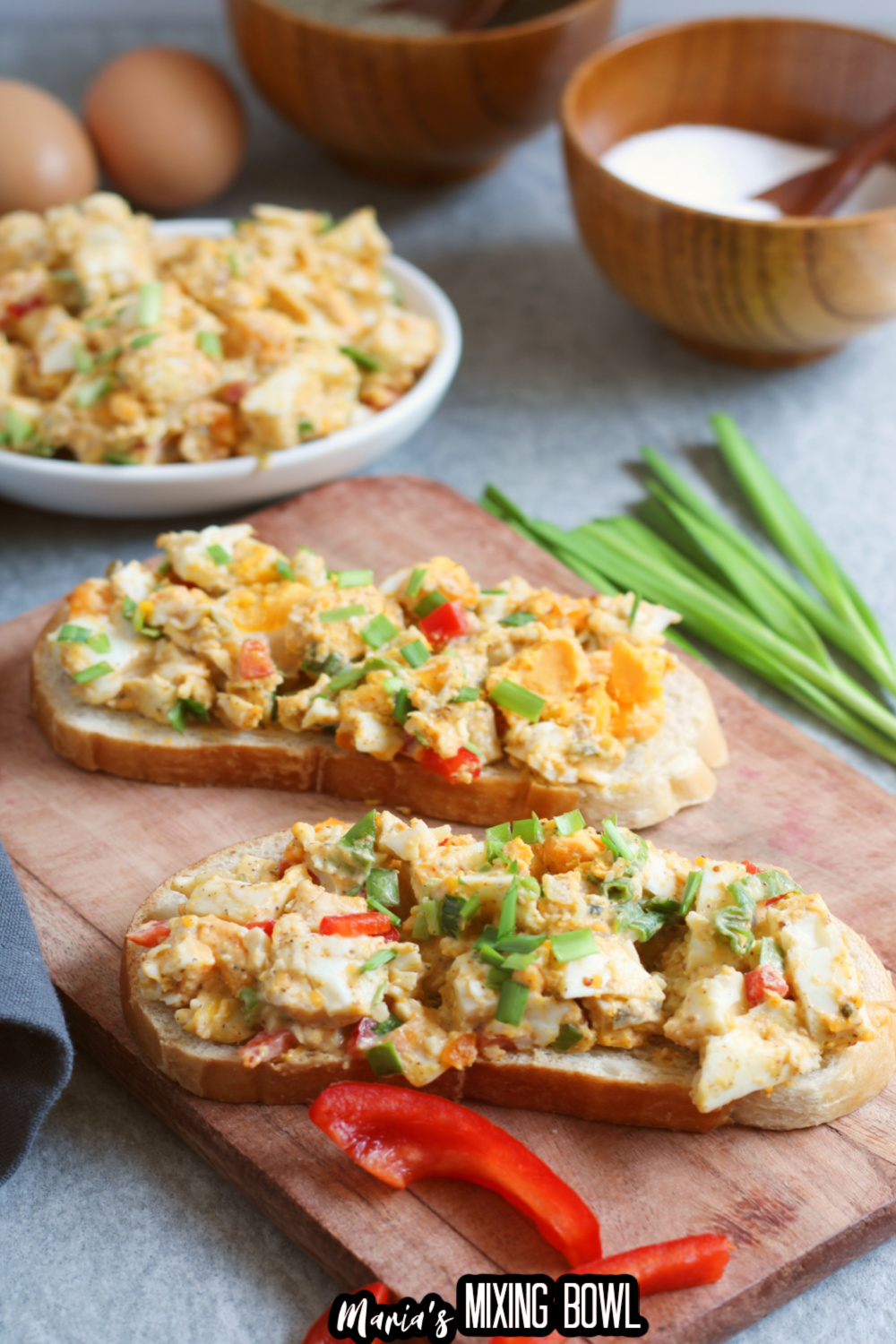 egg salad on two pieces of bread on a wooden cutting board