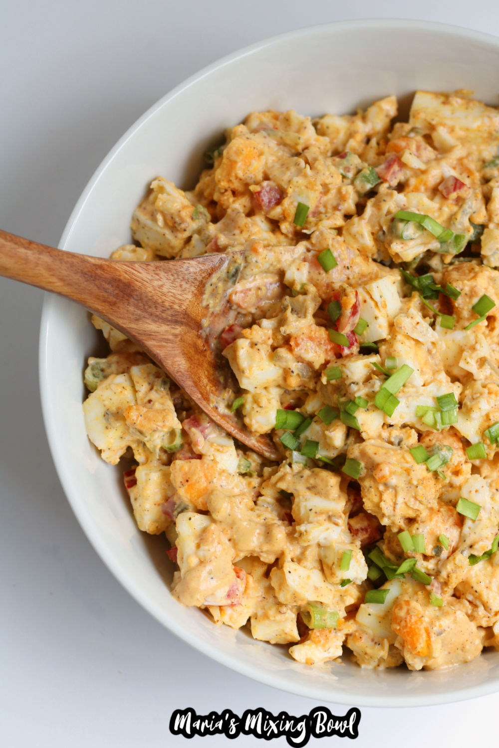egg salad in a white mixing bowl with a bite on a wooden spoon