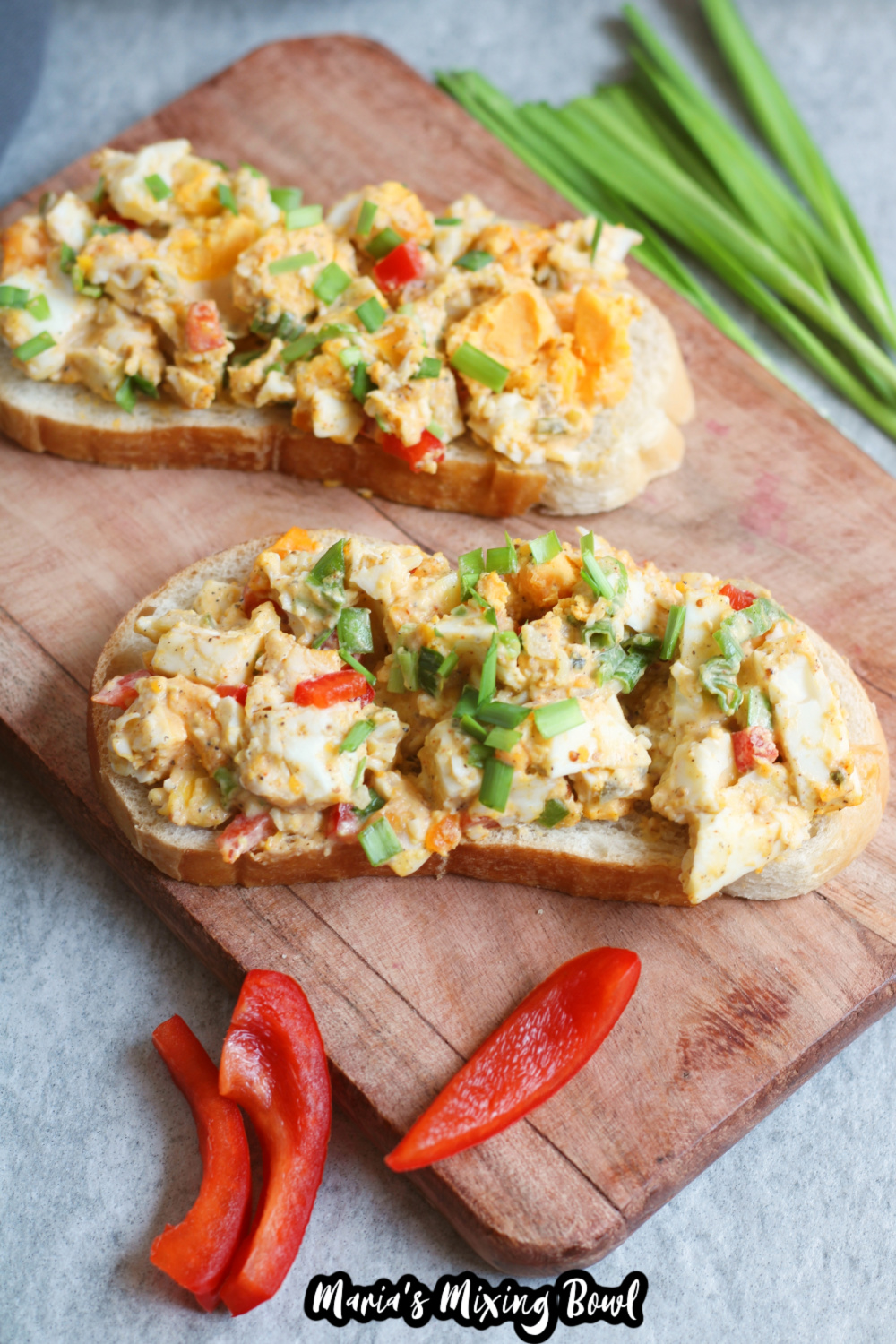 egg salad on two pieces of bread on a wooden cutting board