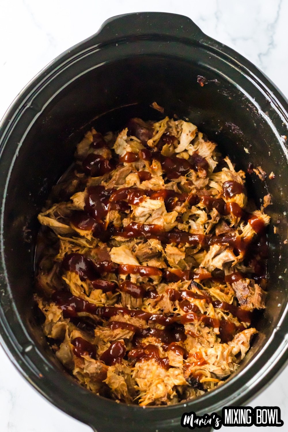 shredded pork in a slow cooker liner topped with bbq sauce