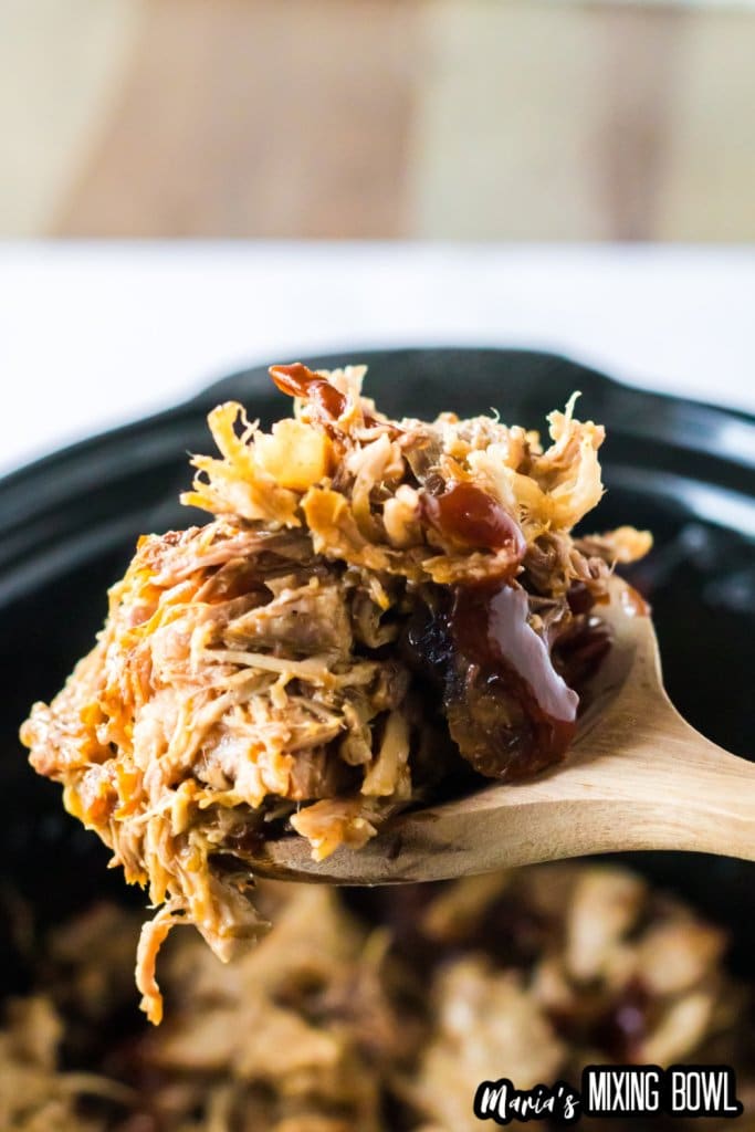 pulled pork on a wooden spoon held in the air above a slow cooker