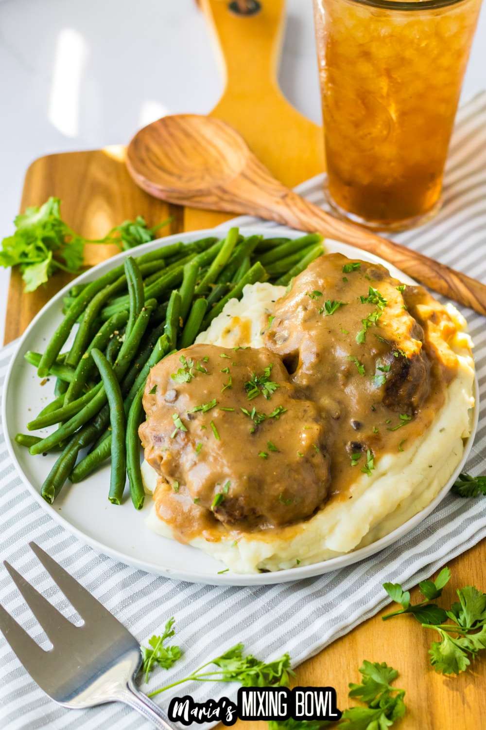 two smothered hamburgers on top of a bed of mashed potatoes with a side of green beans.