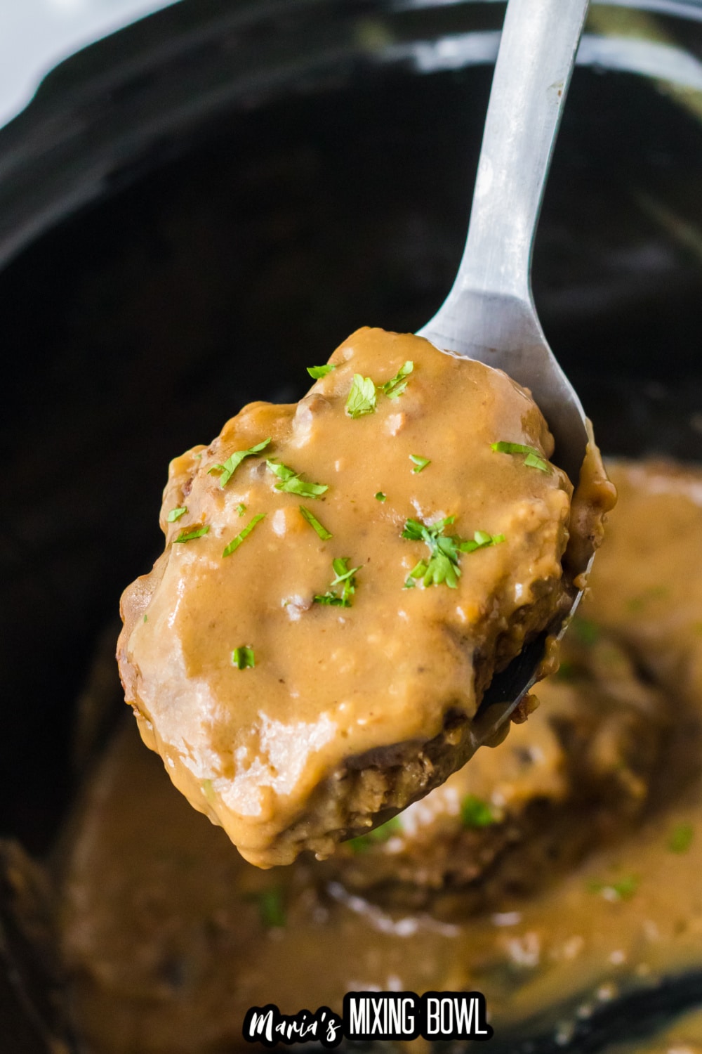 hamburger patty held on a spoon over a slow cooker