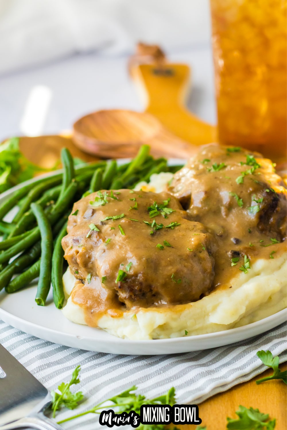 two smothered hamburgers on top of a bed of mashed potatoes with a side of green beans.