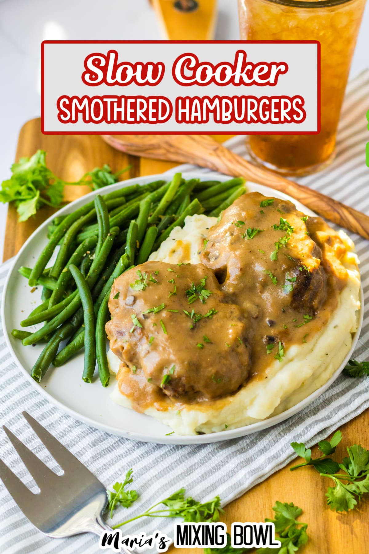 two smothered hamburgers on top of a bed of mashed potatoes with a side of green beans.