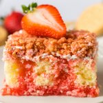 close up of a slice of strawberry crunch poke cake on an off white plate