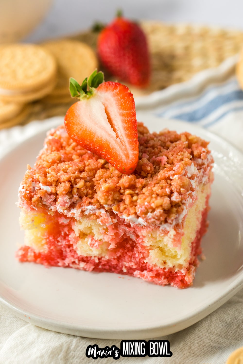 slice of strawberry crunch cake on a white plate topped with a fresh strawberry