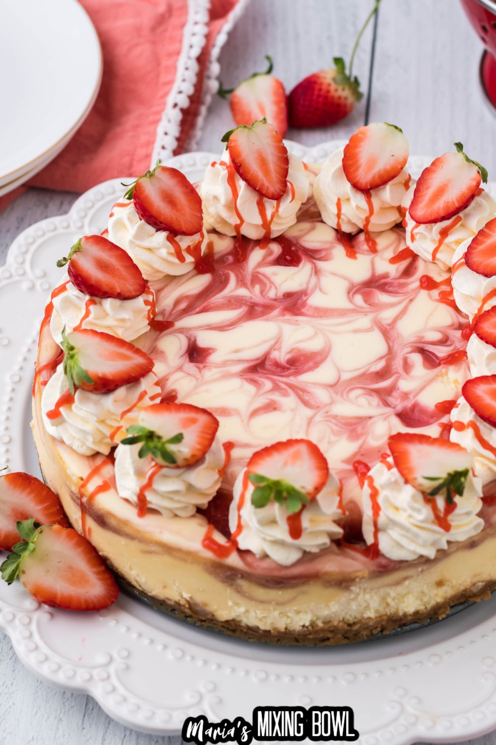 uncut strawberry cheesecake on a white plate topped with fresh strawberries