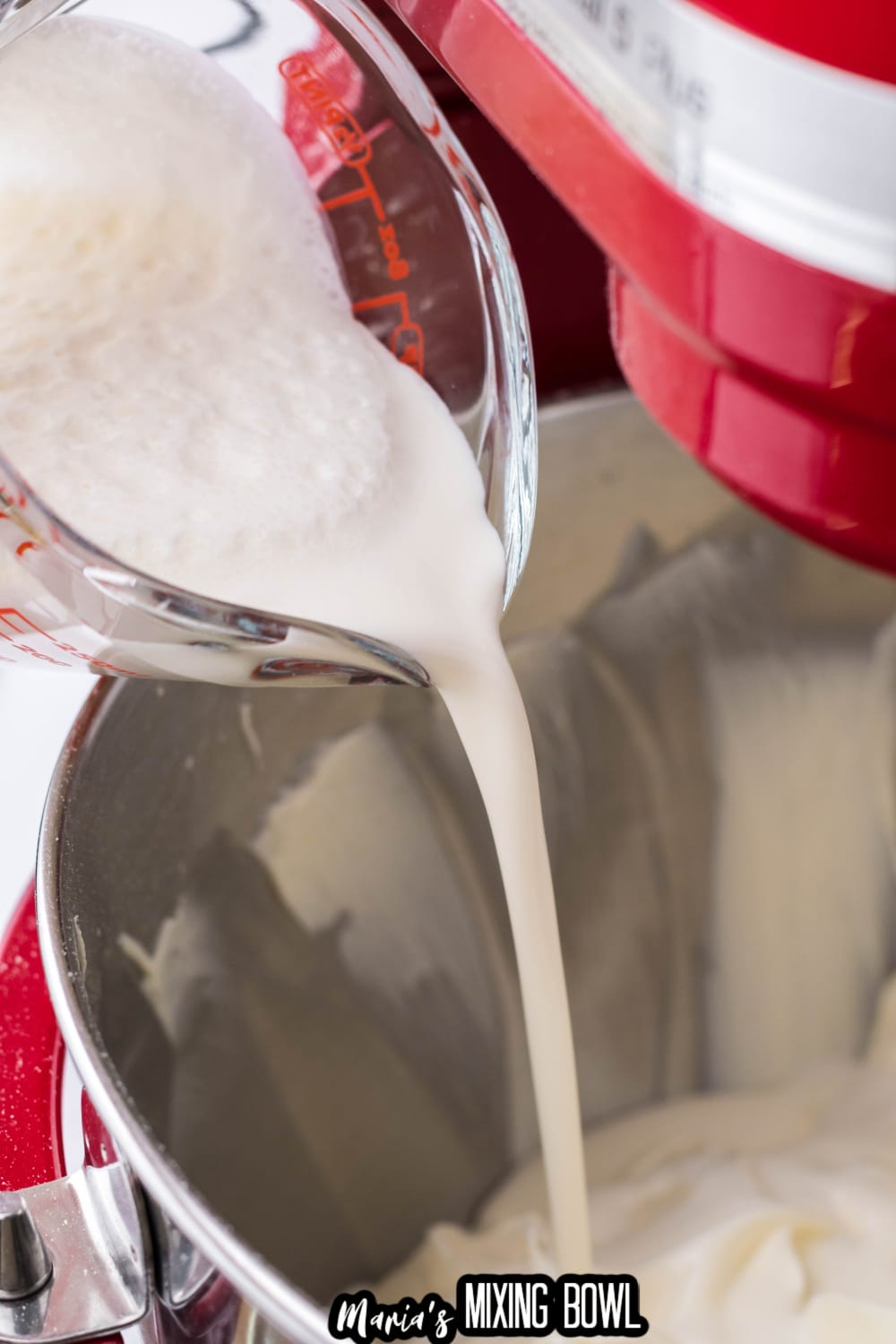 heavy cream being poured into a stainless steel mixing bowl