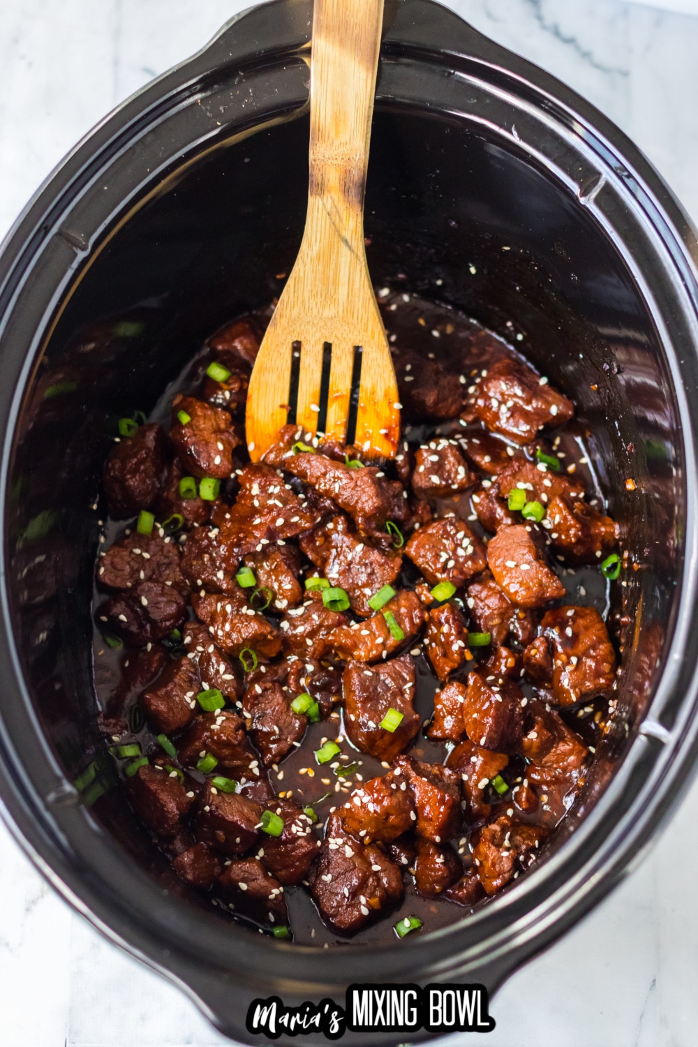 finished garlic butter steak bites in a slow cooker with a slotted wooden spoon