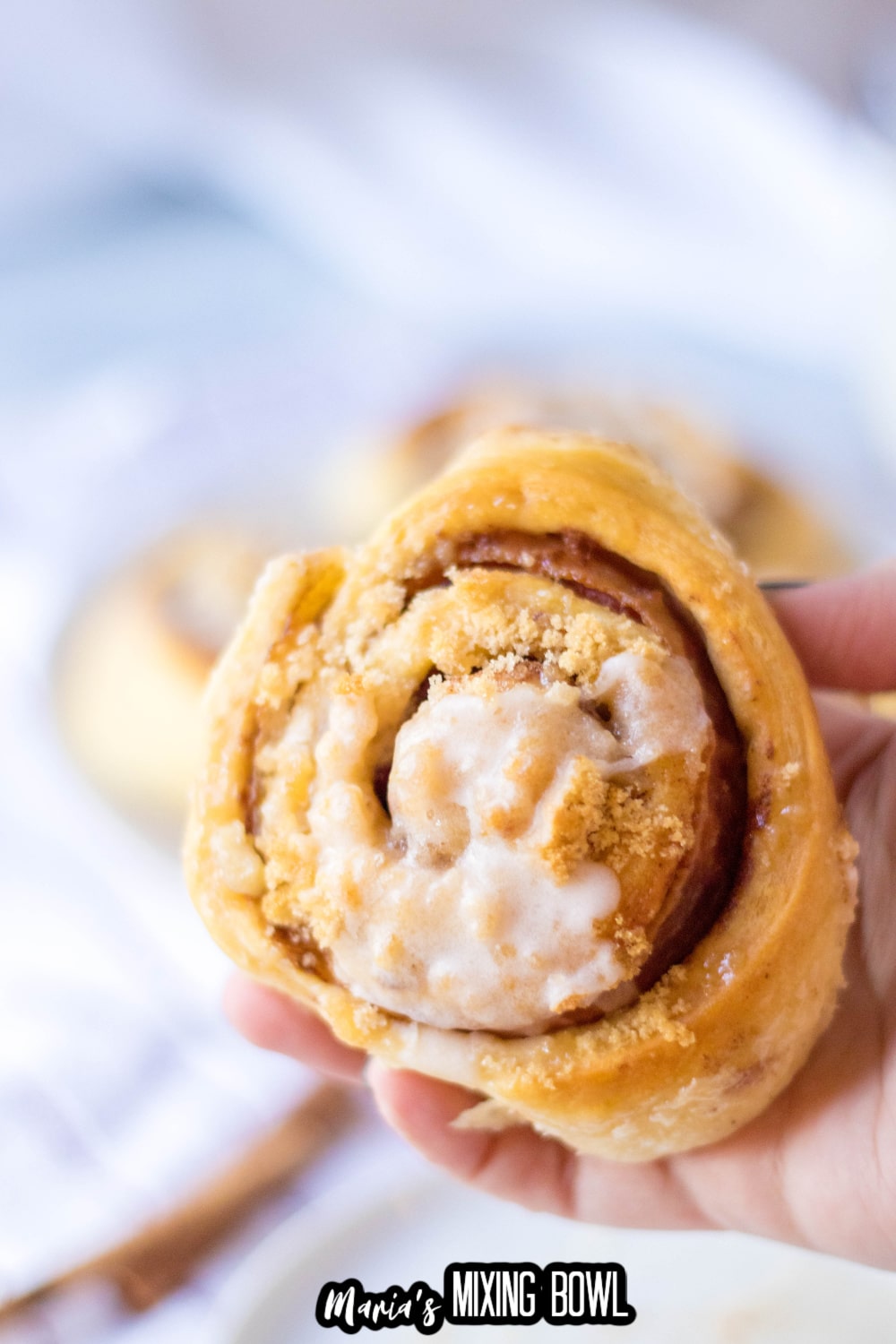 bacon cinnamon roll held in the air in a woman's hand.