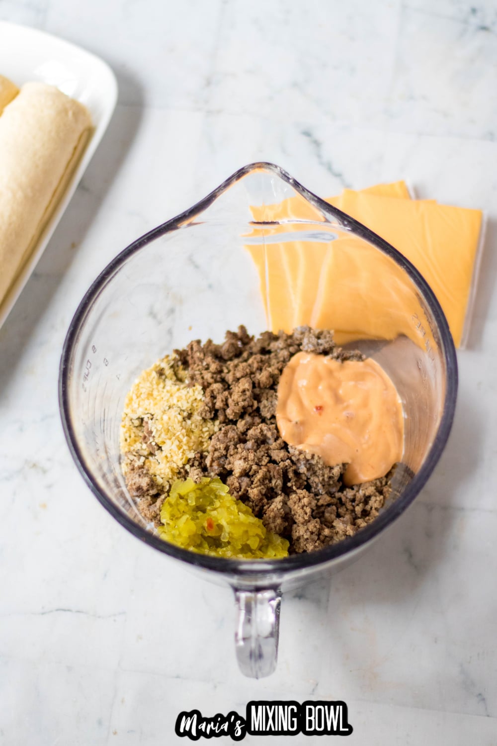 ground beef, big mac sauce, and pickles being mixed together in a glass mixing bowl