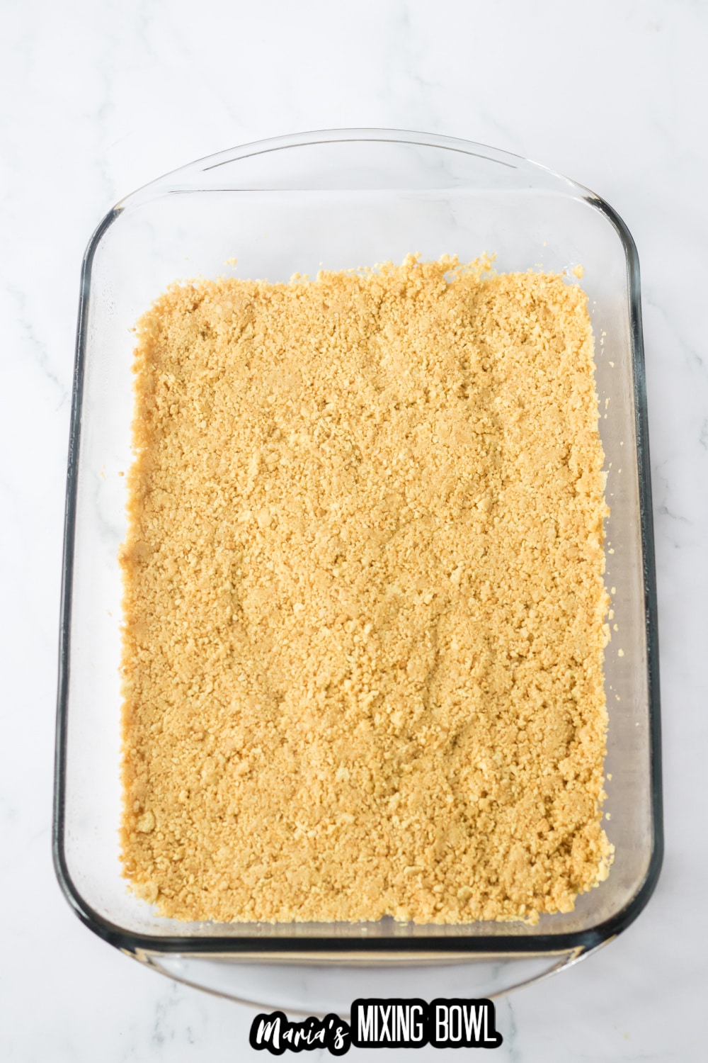 graham cracker crust being pressed into a glass baking dish