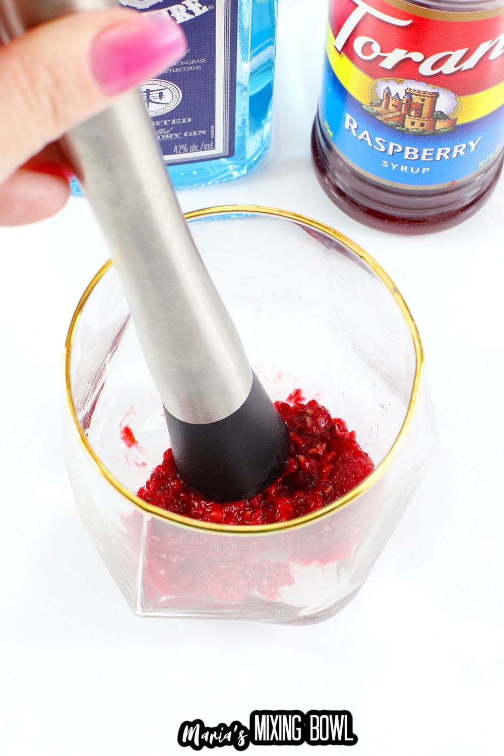 raspberries being muddle in a cocktail glass