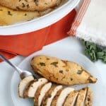 two chicken breasts on a plate. One is sliced and one is whole